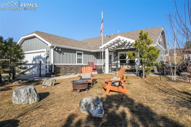 back of house with a fire pit, stone siding, roof with shingles, an attached garage, and board and batten siding