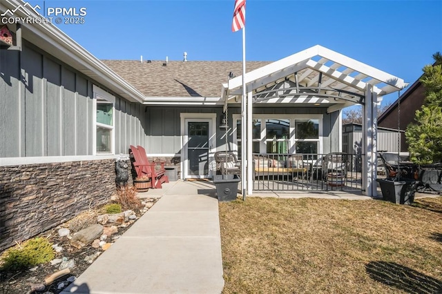 property entrance with roof with shingles, board and batten siding, a patio area, a pergola, and stone siding