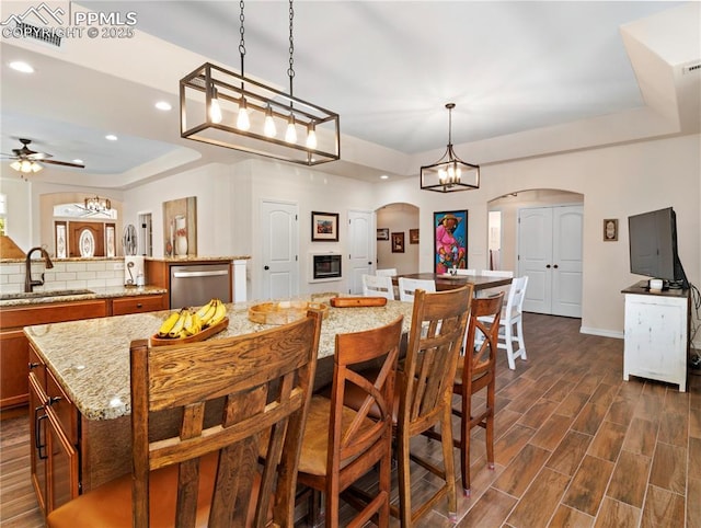 dining room featuring arched walkways, a tray ceiling, dark wood finished floors, recessed lighting, and ceiling fan