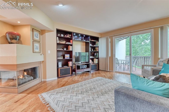 living area with baseboards, a multi sided fireplace, and wood finished floors