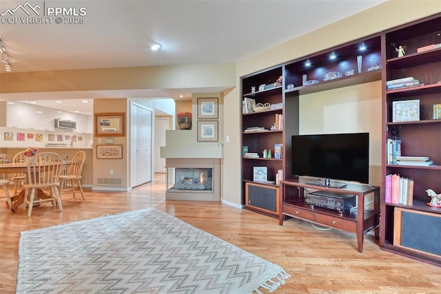 living room featuring built in features, visible vents, a multi sided fireplace, wood finished floors, and baseboards