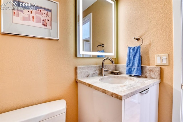 bathroom with toilet, a textured wall, and vanity