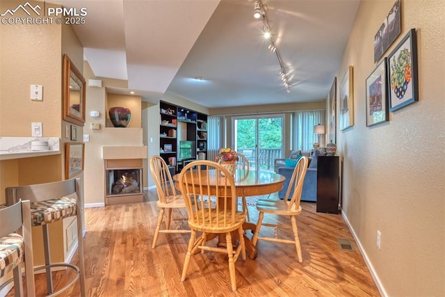 dining space featuring visible vents, a lit fireplace, baseboards, and wood finished floors