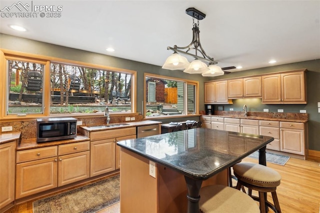 kitchen featuring stainless steel microwave, a sink, a kitchen breakfast bar, light wood finished floors, and recessed lighting