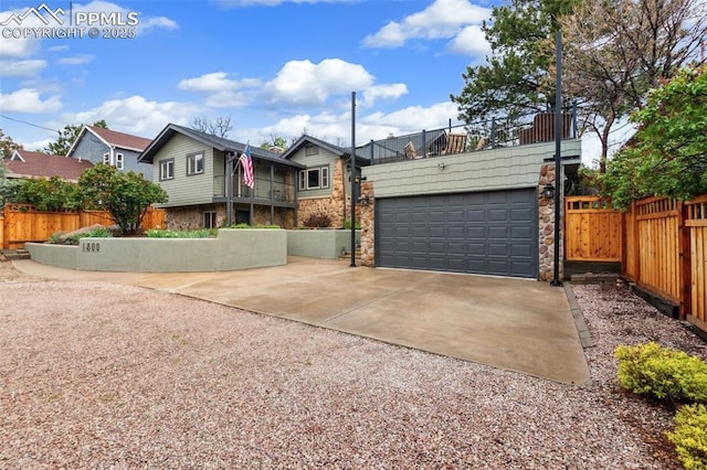 view of front facade with concrete driveway, stone siding, a garage, and fence