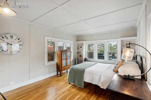 bedroom featuring light wood finished floors, baseboards, ornamental molding, and a decorative wall