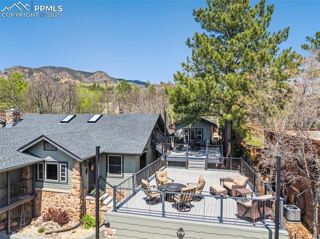 view of front of property featuring roof with shingles, a chimney, a deck with mountain view, stone siding, and outdoor dining space