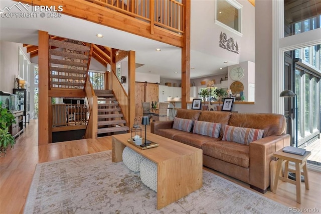 living room featuring a barn door, recessed lighting, a high ceiling, wood finished floors, and stairs