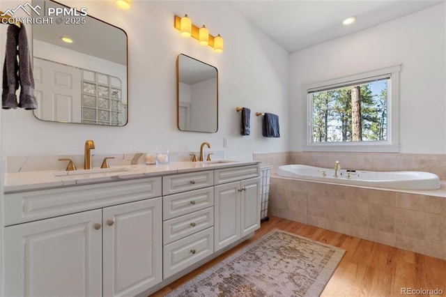 full bath featuring a garden tub, double vanity, wood finished floors, and a sink