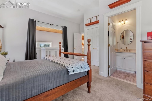 bedroom with vaulted ceiling, ensuite bath, a sink, and light colored carpet