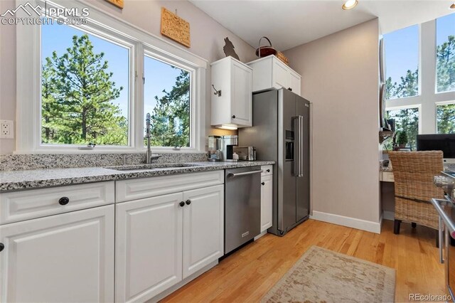 kitchen featuring appliances with stainless steel finishes, plenty of natural light, a sink, and light stone counters