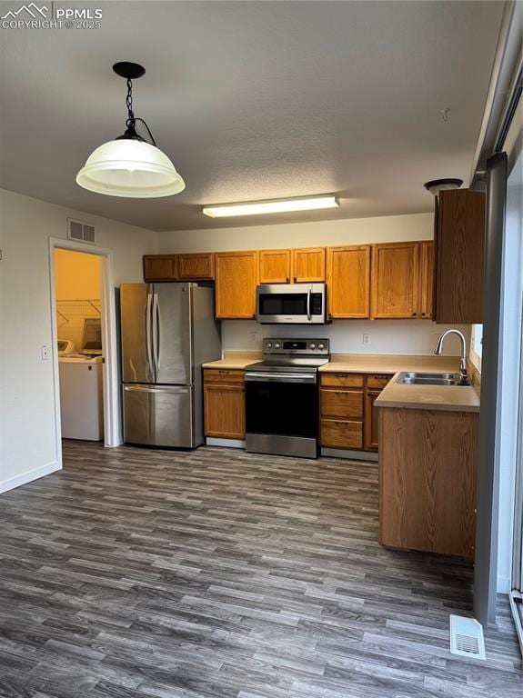 kitchen with washing machine and clothes dryer, stainless steel appliances, visible vents, brown cabinetry, and a sink