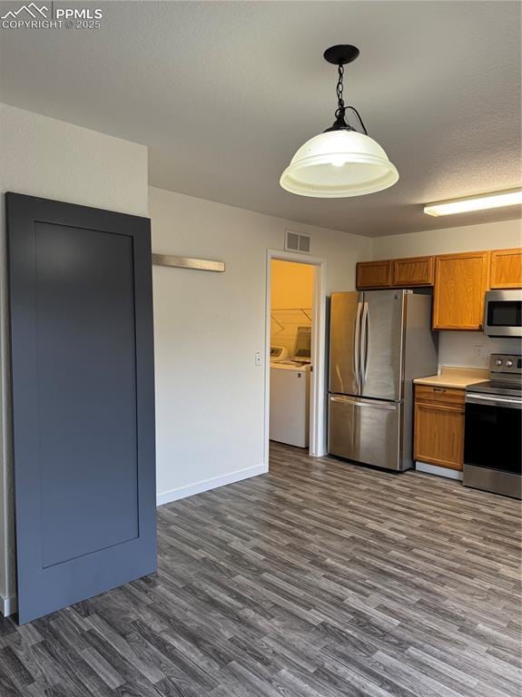 kitchen with dark wood-style flooring, visible vents, appliances with stainless steel finishes, brown cabinetry, and washer and dryer