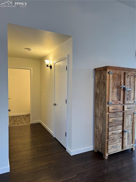 hall with a textured ceiling, baseboards, and wood finished floors