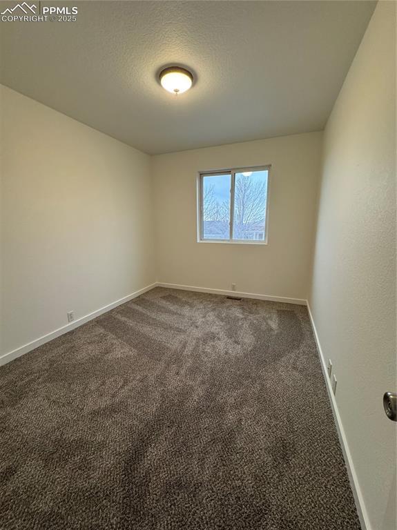 unfurnished room featuring baseboards, dark colored carpet, and a textured ceiling