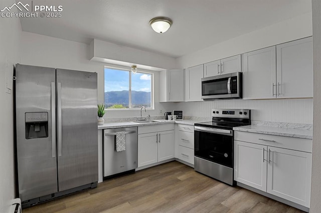 1073 Westmoreland Rd, Colorado Springs, CO 80907 - kitchen featuring appliances with stainless steel finishes, white cabinets, a sink, and light wood-style flooring