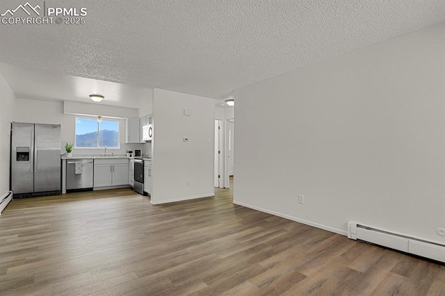 1073 Westmoreland Rd, Colorado Springs, CO 80907 - unfurnished living room with baseboards, wood finished floors, baseboard heating, a textured ceiling, and a sink