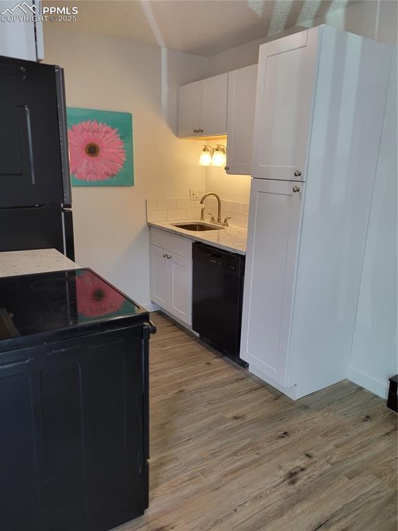 kitchen featuring light wood-style floors, light countertops, black appliances, white cabinetry, and a sink