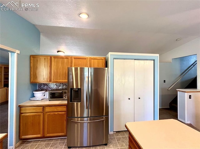 kitchen featuring a toaster, stainless steel fridge with ice dispenser, brown cabinets, light countertops, and backsplash