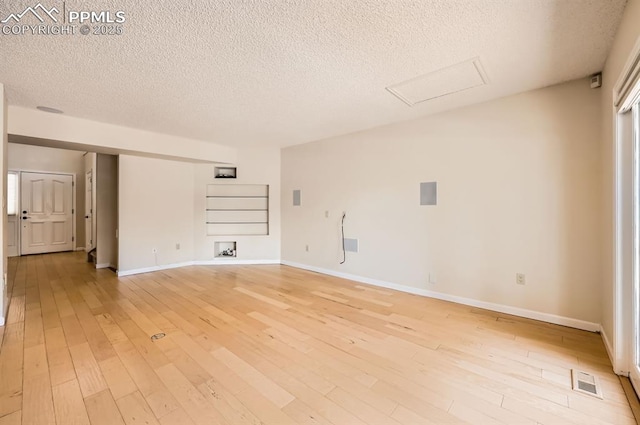 unfurnished room with a textured ceiling, visible vents, baseboards, light wood-style floors, and attic access