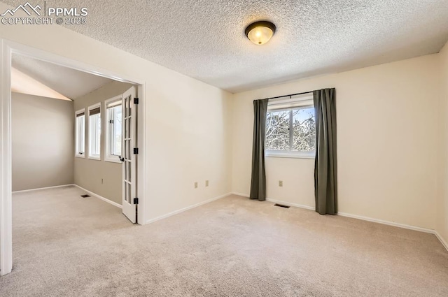 carpeted spare room featuring baseboards, vaulted ceiling, visible vents, and a healthy amount of sunlight