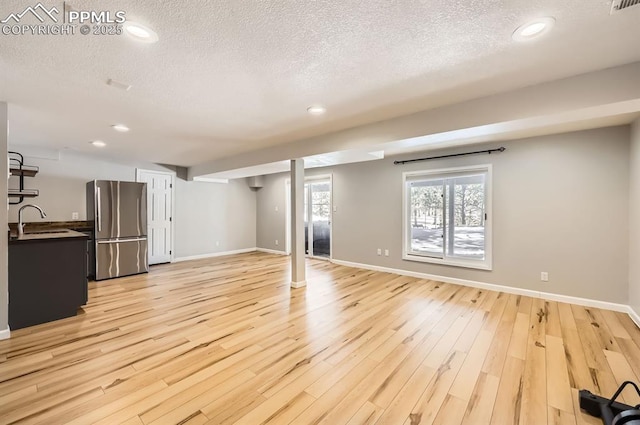 unfurnished living room with light wood-style floors, a sink, a textured ceiling, and baseboards