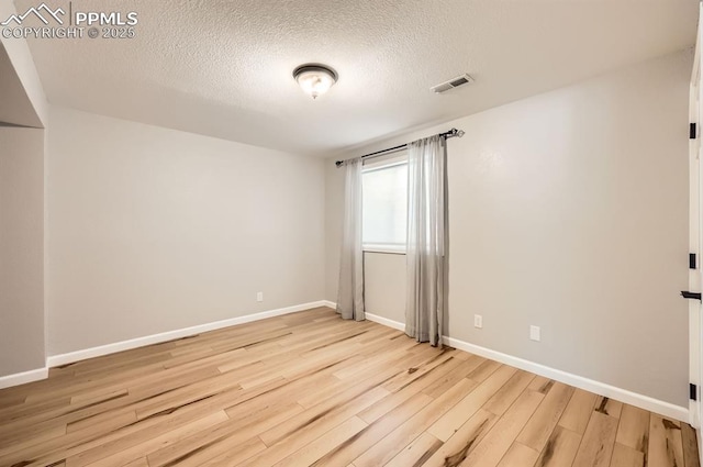 spare room with visible vents, a textured ceiling, baseboards, and wood finished floors