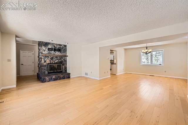 unfurnished living room with a chandelier, a textured ceiling, a stone fireplace, baseboards, and light wood-style floors