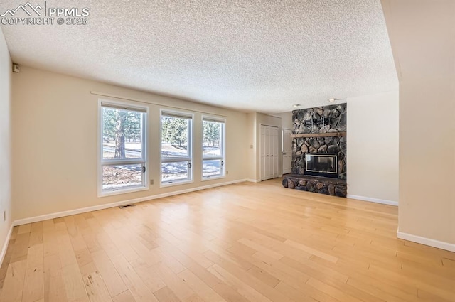 unfurnished living room featuring visible vents, a stone fireplace, a textured ceiling, and light wood-style flooring