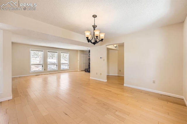 empty room with a chandelier, baseboards, a textured ceiling, and light wood finished floors