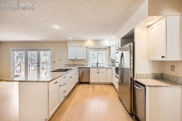 kitchen with light wood finished floors, a peninsula, light stone countertops, stainless steel appliances, and a sink