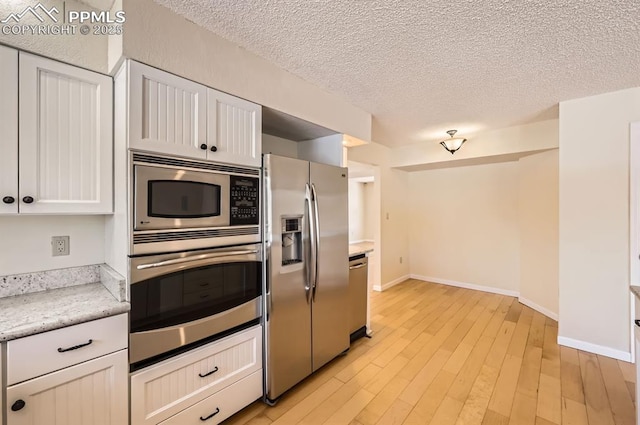 kitchen with stainless steel appliances, light wood-style flooring, white cabinets, a textured ceiling, and baseboards