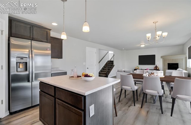 kitchen with light countertops, stainless steel refrigerator with ice dispenser, dark brown cabinets, light wood-style floors, and pendant lighting