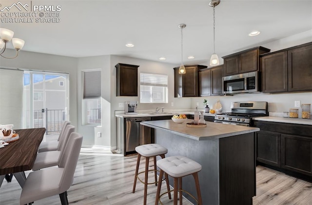 kitchen featuring a breakfast bar area, stainless steel appliances, light countertops, a sink, and dark brown cabinets