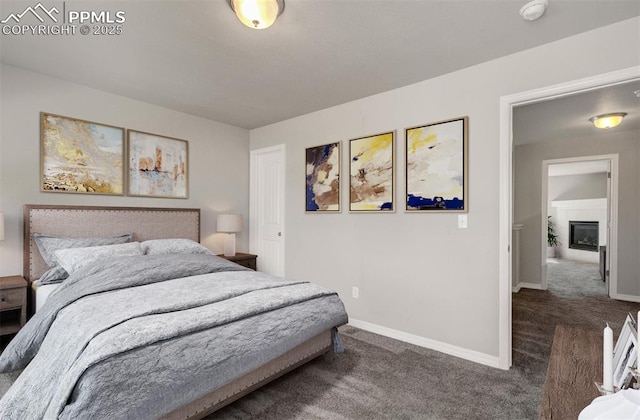 bedroom featuring a glass covered fireplace, carpet flooring, and baseboards