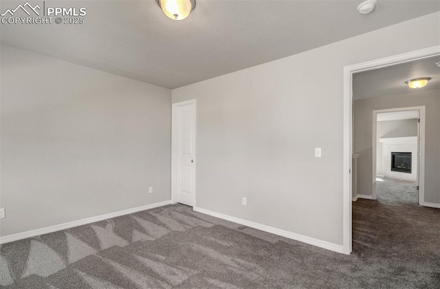 spare room featuring a glass covered fireplace, carpet flooring, and baseboards