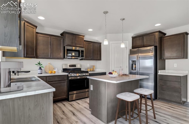 kitchen with appliances with stainless steel finishes, a center island, light countertops, dark brown cabinets, and a sink