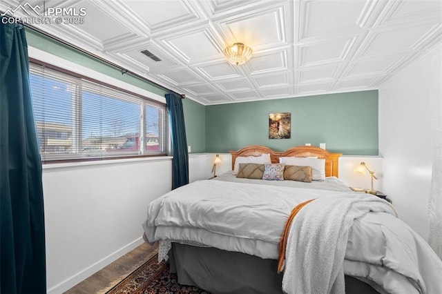 bedroom featuring wood finished floors, an ornate ceiling, and baseboards