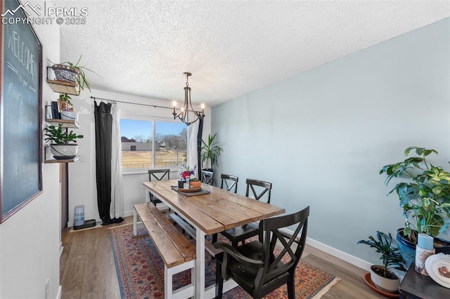 dining area with a textured ceiling, baseboards, wood finished floors, and a notable chandelier