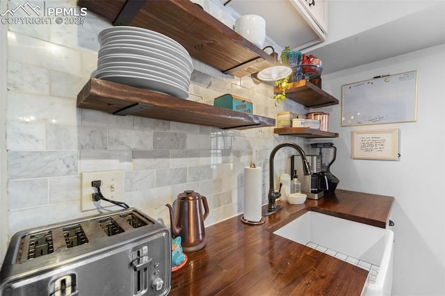 kitchen with a sink, open shelves, wood finished floors, and decorative backsplash