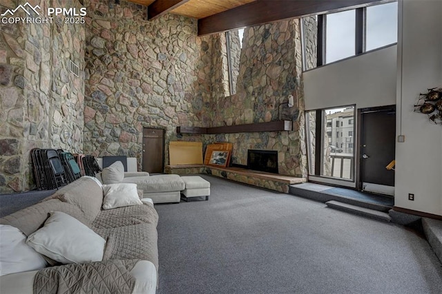 carpeted living room with a healthy amount of sunlight, a towering ceiling, beam ceiling, and a stone fireplace