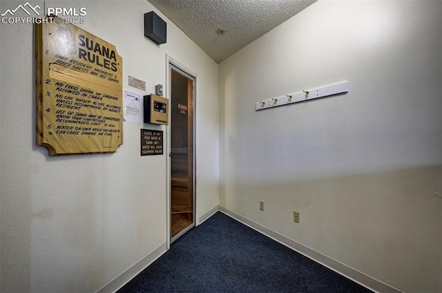 hallway featuring dark colored carpet, a textured ceiling, and baseboards