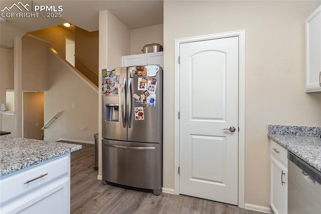 kitchen with appliances with stainless steel finishes, light wood-type flooring, white cabinets, and light stone countertops