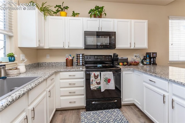 kitchen with light wood-style floors, white cabinets, a sink, light stone countertops, and black appliances