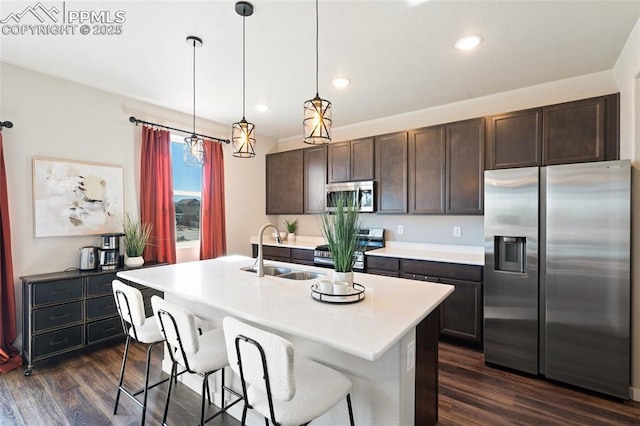 kitchen featuring a center island with sink, stainless steel appliances, dark wood-type flooring, a sink, and dark brown cabinetry