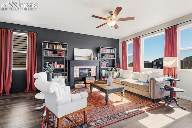 living area featuring ceiling fan, a stone fireplace, wood finished floors, and baseboards