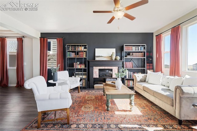 living area with plenty of natural light, a ceiling fan, wood finished floors, and a stone fireplace