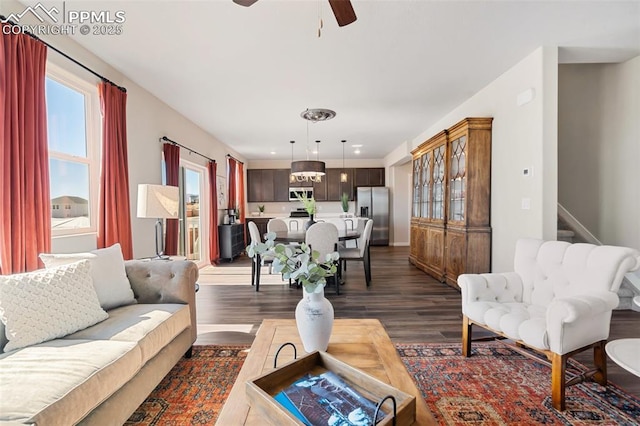 living area with baseboards, stairs, a ceiling fan, and dark wood-style flooring