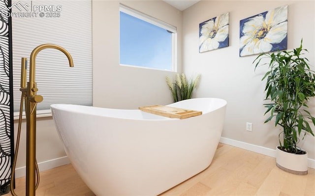 bathroom with a freestanding bath, baseboards, and wood finished floors