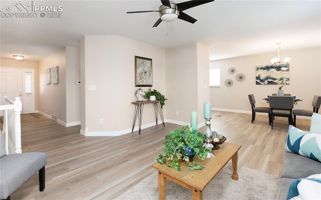 living area featuring light wood-type flooring, baseboards, and ceiling fan with notable chandelier